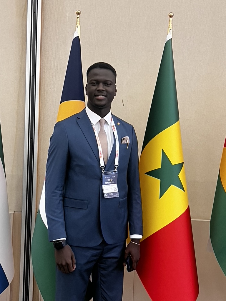 Amath Abdoul Aziz Mbaye, fondateur de Coral Consulting, en tenue professionnelle devant le drapeau du Sénégal